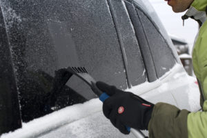 Ein Mann benutzt einen Eiskratzer für sein Auto.