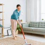 eine Frau saugt mit einem kabellosen Staubsauger den Teppich