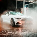 Ein weißes Auto, welches in der Dunkelheit mit Wasser besprüht wird.