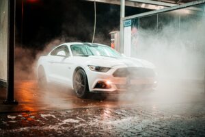 Ein weißes Auto, welches in der Dunkelheit mit Wasser besprüht wird.