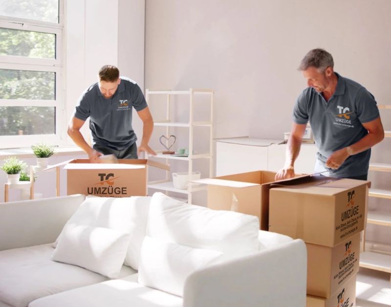 Zwei Mitarbeiter packen Umzugskartons in einer hellen Wohnung.
